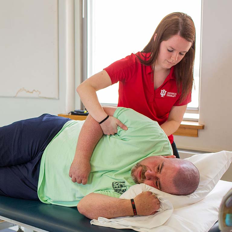 A student helps a patient who is laying on his side.